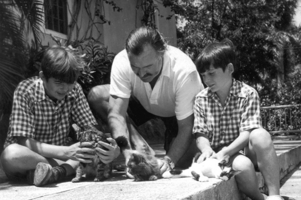 Ernest Hemingway plays with cats alongside his sons.